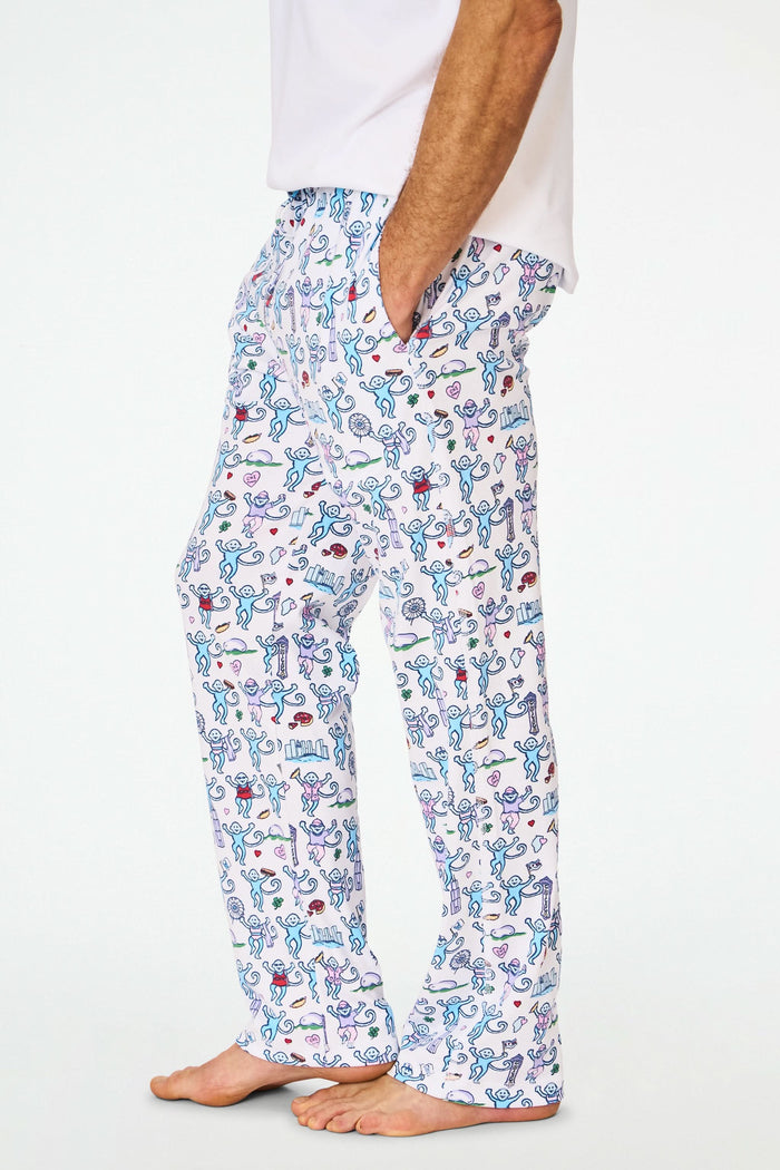 A person stands barefoot in cozy Roller Rabbit Mens Chicago Monkey Simon Pants, featuring a colorful print, paired with a plain white T-shirt. Only the lower half of the body is visible against a white background.