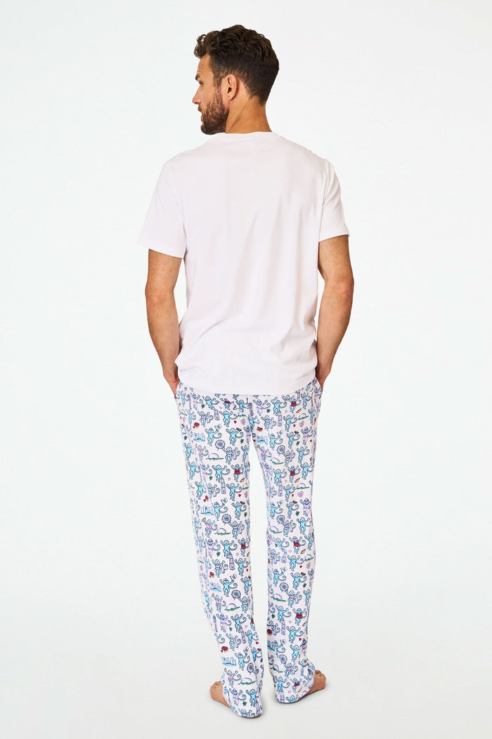 A person stands barefoot in cozy Roller Rabbit Mens Chicago Monkey Simon Pants, featuring a colorful print, paired with a plain white T-shirt. Only the lower half of the body is visible against a white background.