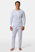 A man stands barefoot, smiling in Roller Rabbit’s Mens Hearts Spencer Pajamas. This matching set has a white background with small blue and red heart patterns. Made of 100 Pima cotton, the pajama top features comfy henley-style buttons.