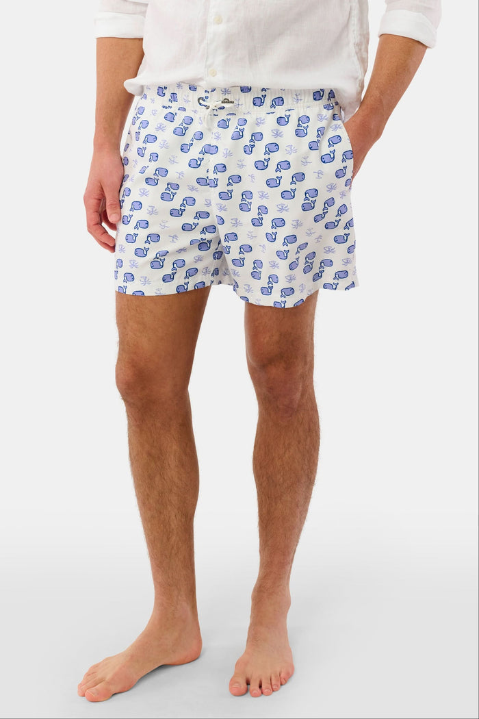 A person wearing the Roller Rabbit Mens Moby Swim Trunk—made from quick-dry polyester with a mesh-lined brief and a blue boxing glove pattern—stands barefoot against a white background.