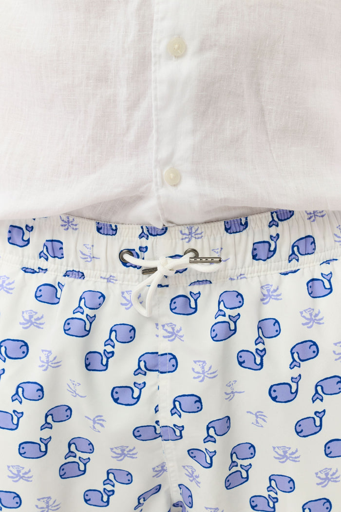 A person wearing the Roller Rabbit Mens Moby Swim Trunk—made from quick-dry polyester with a mesh-lined brief and a blue boxing glove pattern—stands barefoot against a white background.