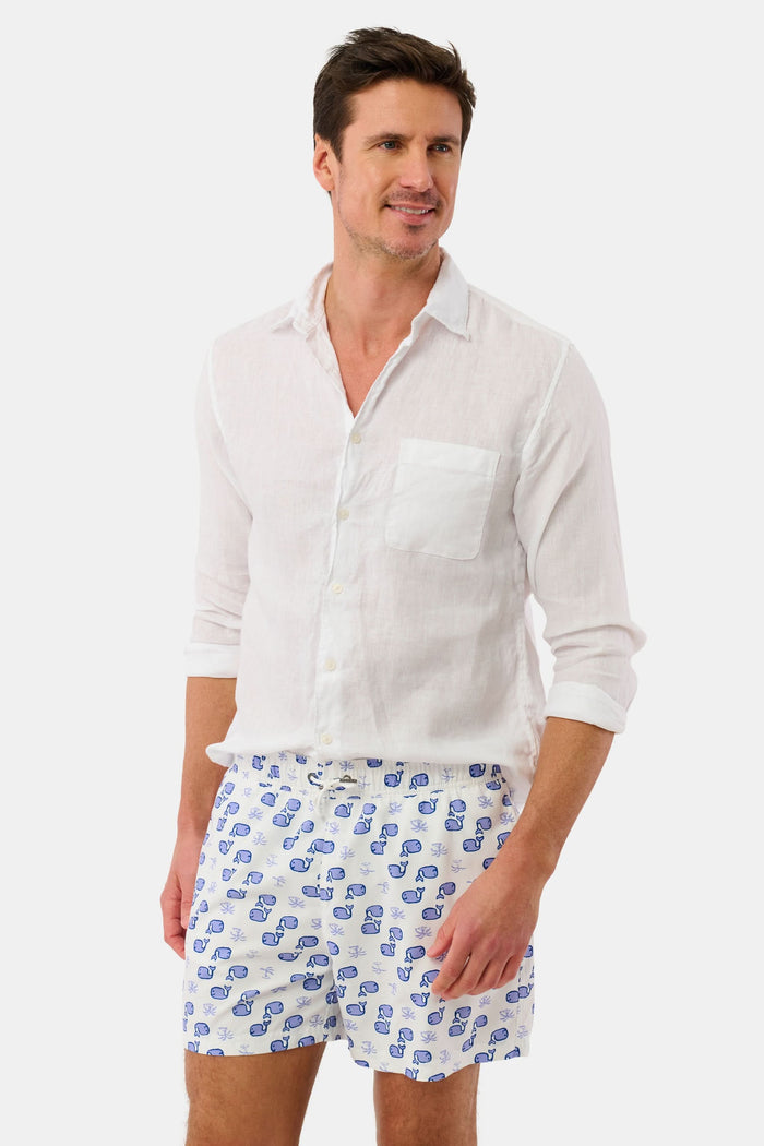 A person wearing the Roller Rabbit Mens Moby Swim Trunk—made from quick-dry polyester with a mesh-lined brief and a blue boxing glove pattern—stands barefoot against a white background.