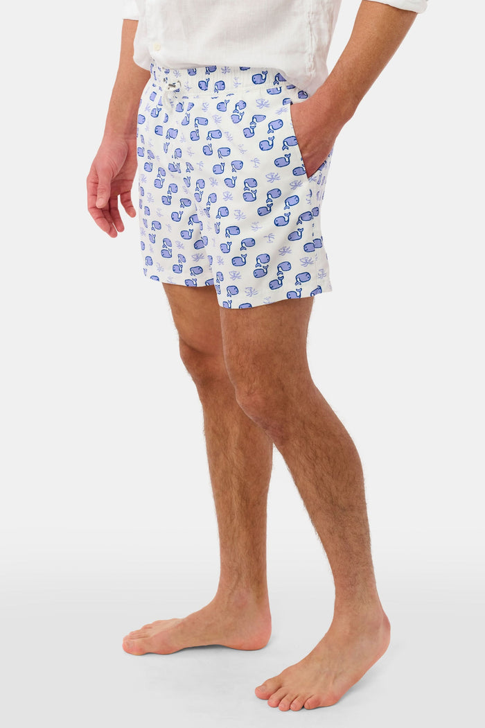 A person wearing the Roller Rabbit Mens Moby Swim Trunk—made from quick-dry polyester with a mesh-lined brief and a blue boxing glove pattern—stands barefoot against a white background.