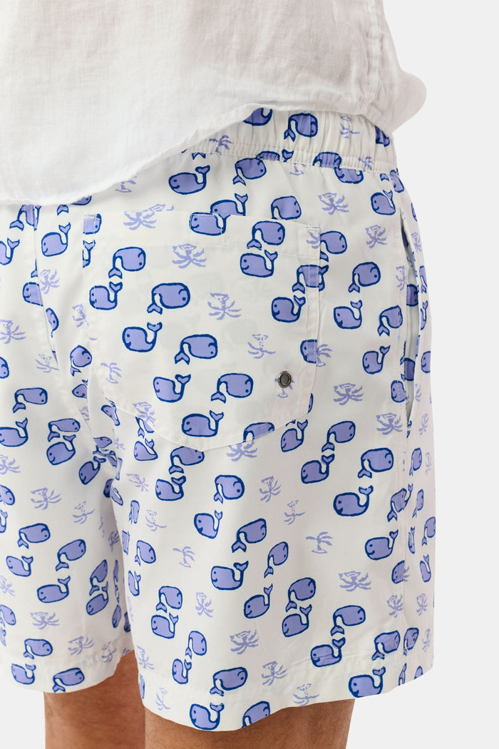 A person wearing the Roller Rabbit Mens Moby Swim Trunk—made from quick-dry polyester with a mesh-lined brief and a blue boxing glove pattern—stands barefoot against a white background.