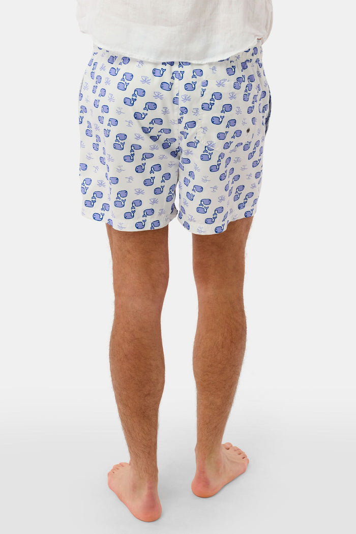 A person wearing the Roller Rabbit Mens Moby Swim Trunk—made from quick-dry polyester with a mesh-lined brief and a blue boxing glove pattern—stands barefoot against a white background.
