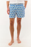A person wearing a white shirt and Roller Rabbit’s MENS MONKEY SWIM TRUNK stands barefoot against a white background. The swim trunks showcase a playful, abstract blue-and-white design and are crafted as quick-dry swimwear with comfortable mesh-lined briefs.