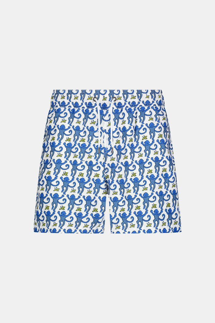 A person wearing a white shirt and Roller Rabbit’s MENS MONKEY SWIM TRUNK stands barefoot against a white background. The swim trunks showcase a playful, abstract blue-and-white design and are crafted as quick-dry swimwear with comfortable mesh-lined briefs.
