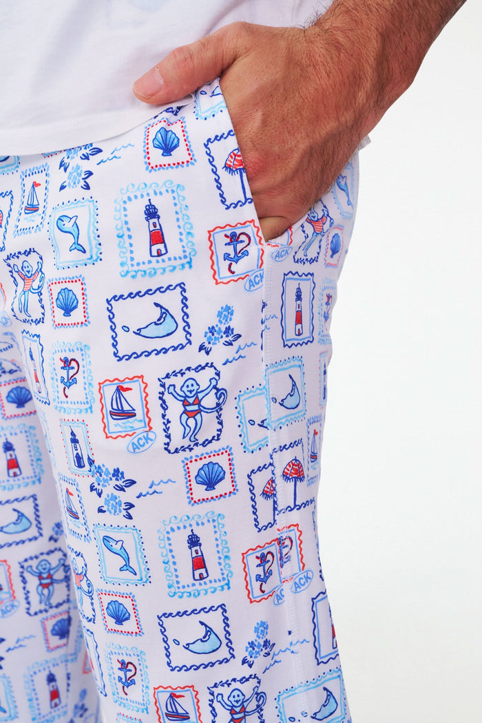 A person wears Roller Rabbit's Mens Nantucket Memories Simon Pant—white pajama pants with blue and red nautical prints like lighthouses, whales, and ship wheels. Only the lower half of the body is shown in the photo.