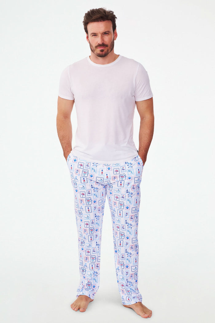 A person wears Roller Rabbit's Mens Nantucket Memories Simon Pant—white pajama pants with blue and red nautical prints like lighthouses, whales, and ship wheels. Only the lower half of the body is shown in the photo.