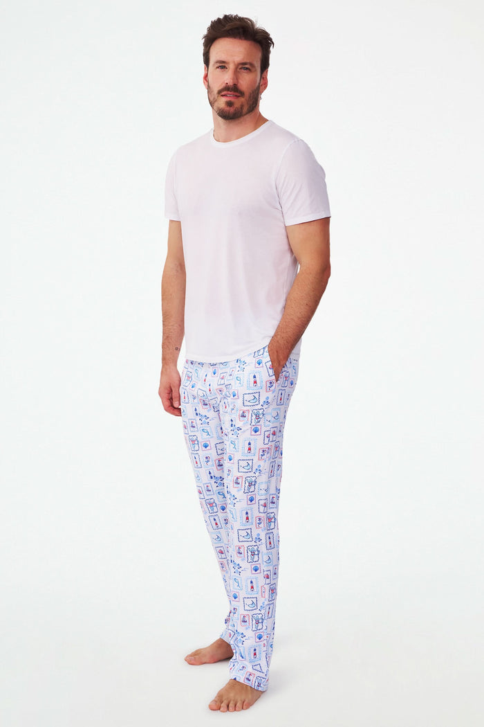 A person wears Roller Rabbit's Mens Nantucket Memories Simon Pant—white pajama pants with blue and red nautical prints like lighthouses, whales, and ship wheels. Only the lower half of the body is shown in the photo.