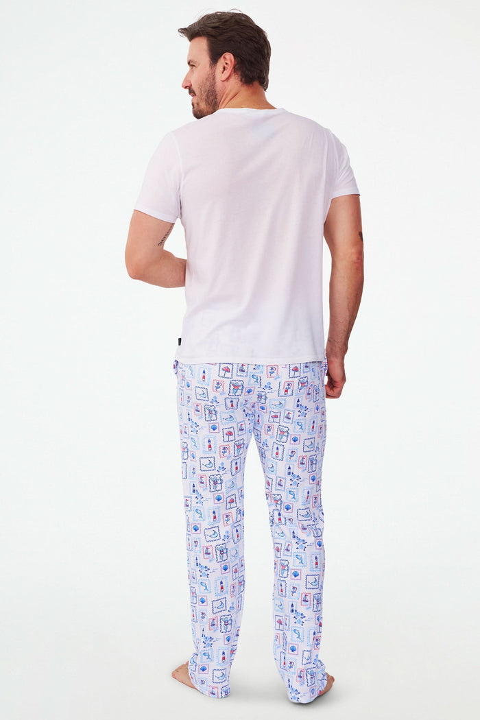 A person wears Roller Rabbit's Mens Nantucket Memories Simon Pant—white pajama pants with blue and red nautical prints like lighthouses, whales, and ship wheels. Only the lower half of the body is shown in the photo.