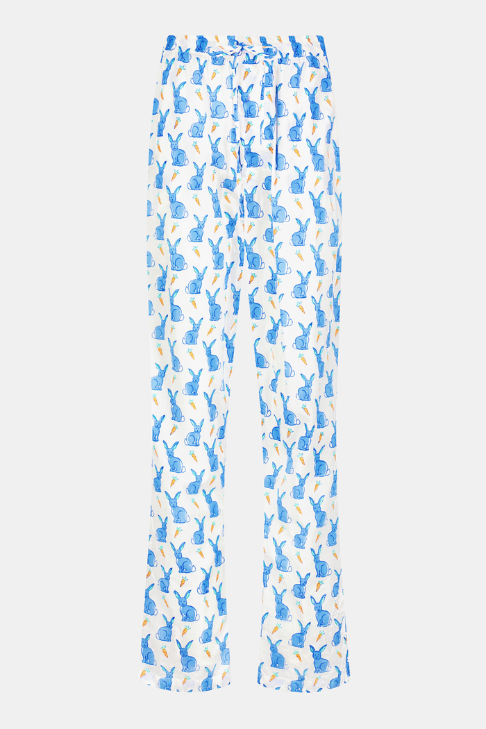 A person stands barefoot against a white background, wearing Roller Rabbit's Mens Romy the Rabbit Jon Pant—white vintage cotton pants with a blue and orange bunny print—one hand in their pocket, the other at their side.