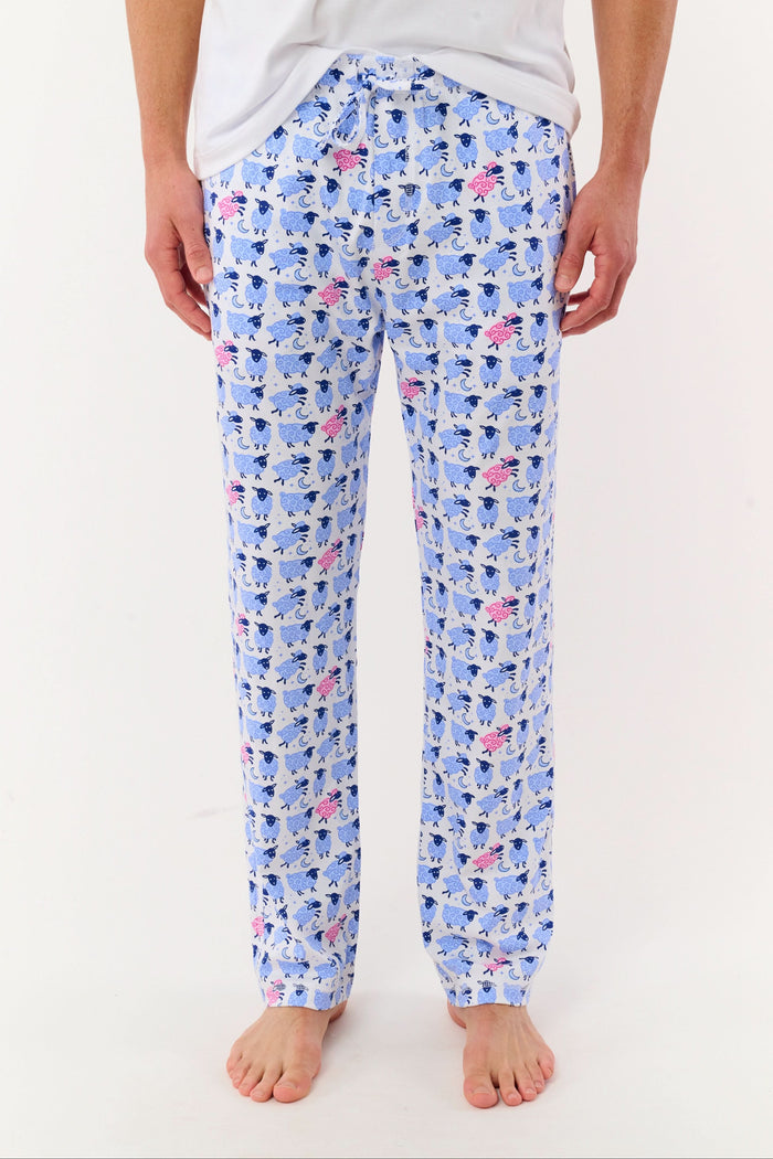 A person models the lower half of the Roller Rabbit Mens Sammy The Sheep Simon Pant—a relaxed fit PJ pant featuring a blue and pink sheep print—while standing barefoot on a white background.