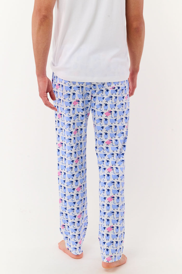 A person models the lower half of the Roller Rabbit Mens Sammy The Sheep Simon Pant—a relaxed fit PJ pant featuring a blue and pink sheep print—while standing barefoot on a white background.