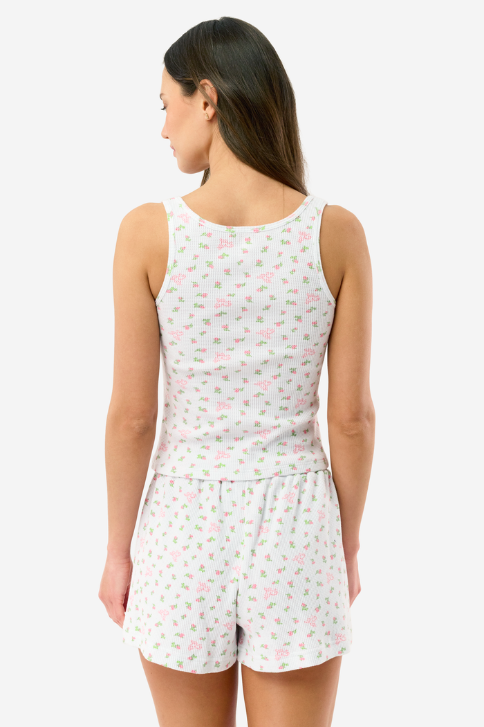 A woman stands barefoot against a white background, wearing the Roller Rabbit Mini Monkey Blossom Cherry Tank Set—a matching white tank top and shorts with a small floral pattern.