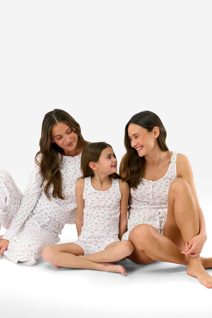 A woman stands barefoot against a white background, wearing the Roller Rabbit Mini Monkey Blossom Cherry Tank Set—a matching white tank top and shorts with a small floral pattern.