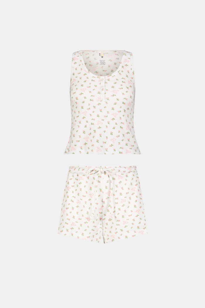 A woman stands barefoot against a white background, wearing the Roller Rabbit Mini Monkey Blossom Cherry Tank Set—a matching white tank top and shorts with a small floral pattern.