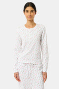 A woman wears the Mini Monkey Blossom Rosemary Top by Roller Rabbit, featuring a white pima cotton fabric with a small pink floral pattern, standing facing forward against a light background with her hands at her sides.