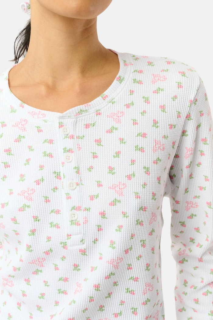 A woman wears the Mini Monkey Blossom Rosemary Top by Roller Rabbit, featuring a white pima cotton fabric with a small pink floral pattern, standing facing forward against a light background with her hands at her sides.