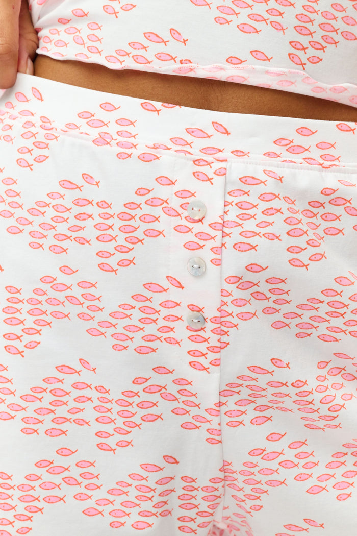 A person is wearing the Roller Rabbit Minnows Sullivan Shortie—a matching slumber party PJ set with a white base, pink zig-zag minnow print, sleeveless top, high-waisted shorts, wavy hem, and front buttons.