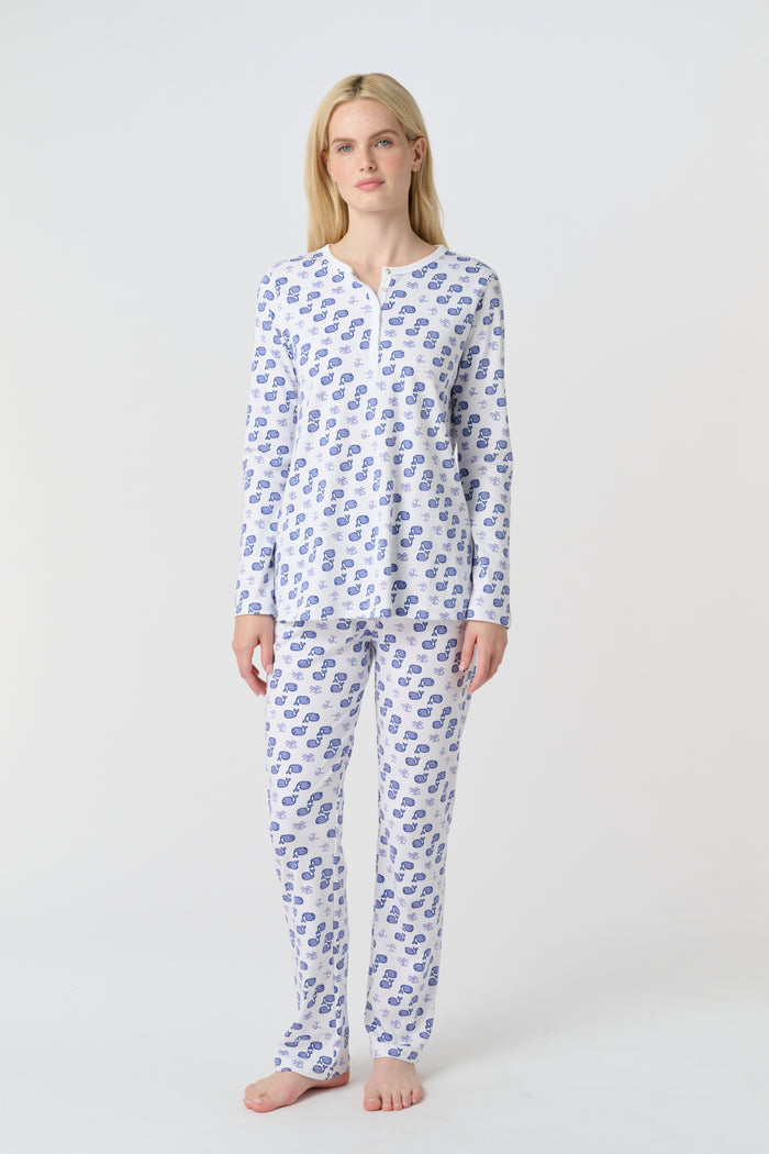 A woman with long blonde hair wears the Roller Rabbit Moby Pajamas, featuring a blue and white repeating print, as she stands barefoot against a plain white background.