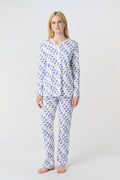 A woman with long blonde hair wears the Roller Rabbit Moby Pajamas, featuring a blue and white repeating print, as she stands barefoot against a plain white background.