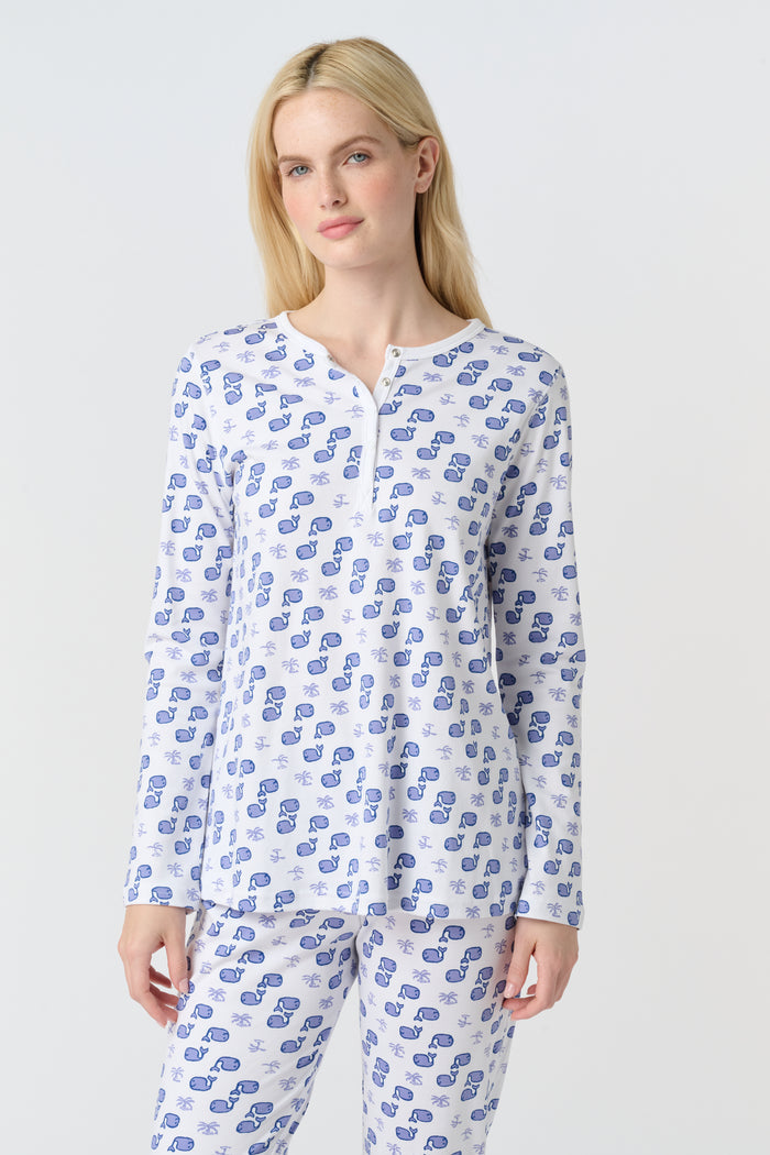 A woman with long blonde hair wears the Roller Rabbit Moby Pajamas, featuring a blue and white repeating print, as she stands barefoot against a plain white background.