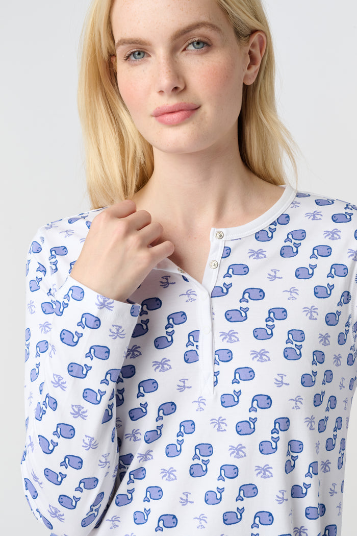 A woman with long blonde hair wears the Roller Rabbit Moby Pajamas, featuring a blue and white repeating print, as she stands barefoot against a plain white background.