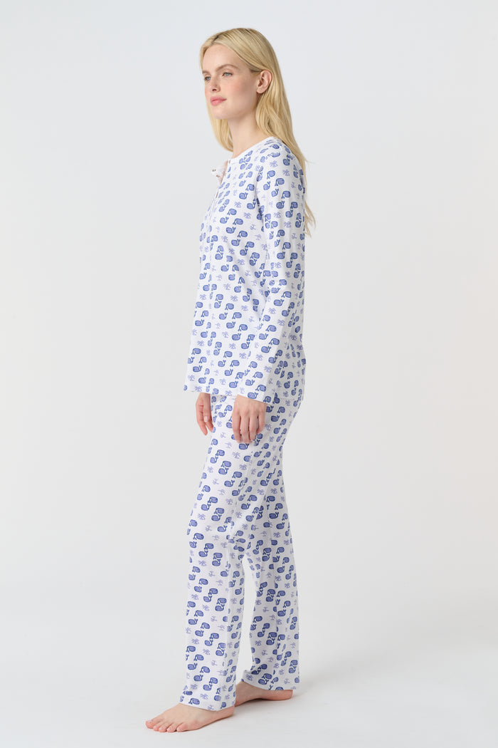 A woman with long blonde hair wears the Roller Rabbit Moby Pajamas, featuring a blue and white repeating print, as she stands barefoot against a plain white background.