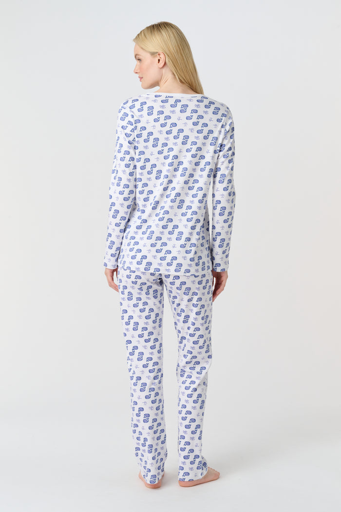 A woman with long blonde hair wears the Roller Rabbit Moby Pajamas, featuring a blue and white repeating print, as she stands barefoot against a plain white background.