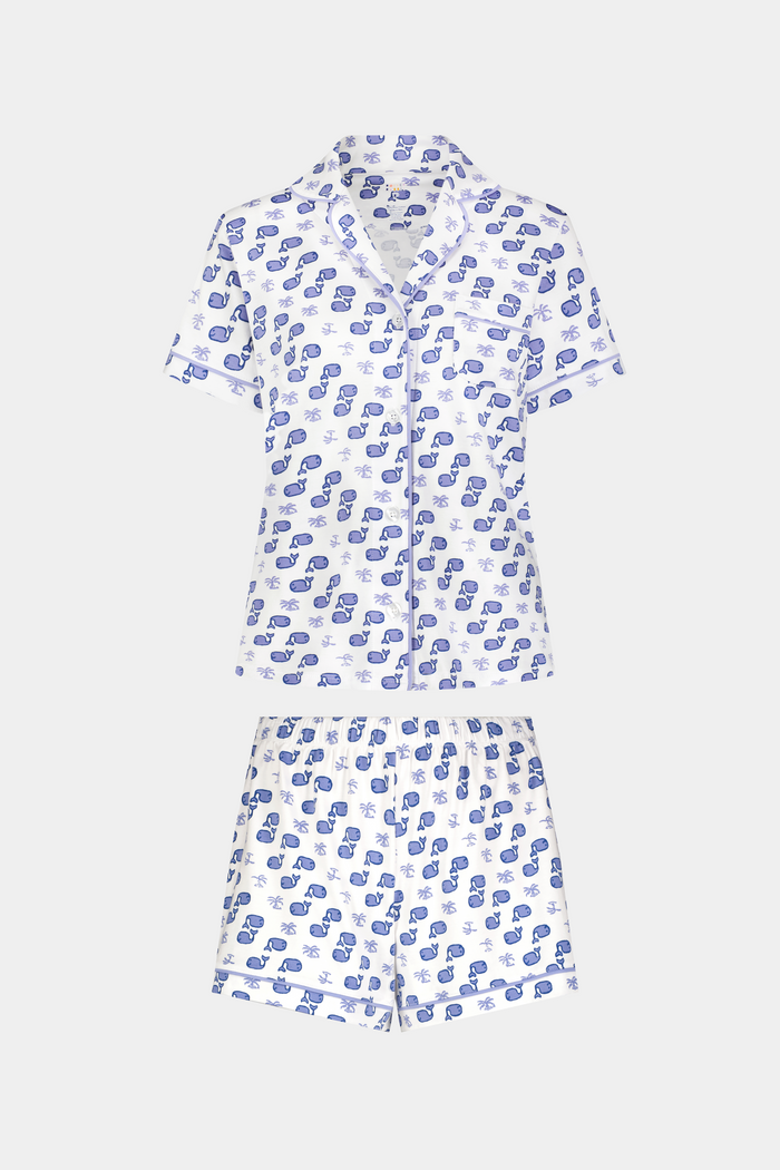 A woman with light brown hair and a gentle smile stands against a plain background, wearing Roller Rabbit's Moby Polo Pajamas—a women's short-sleeve sleepwear set featuring a whale print and crafted from soft Pima cotton.