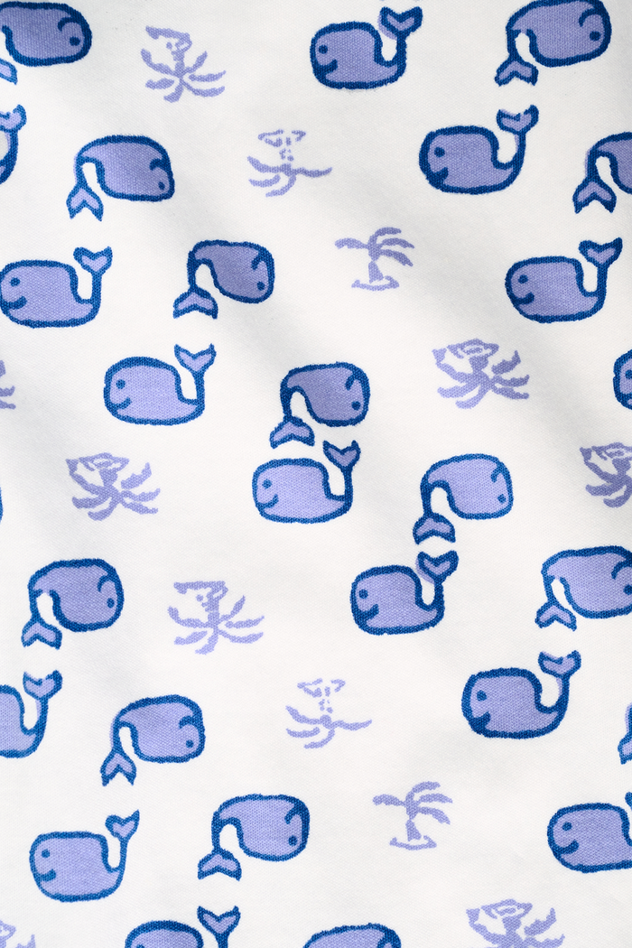 A woman stands barefoot in the Roller Rabbit Moby Long Sleeve Polo Pajamas, featuring a blue geometric-patterned white top and pants. Made from soft pima cotton, the comfy set is shown against a plain white background.