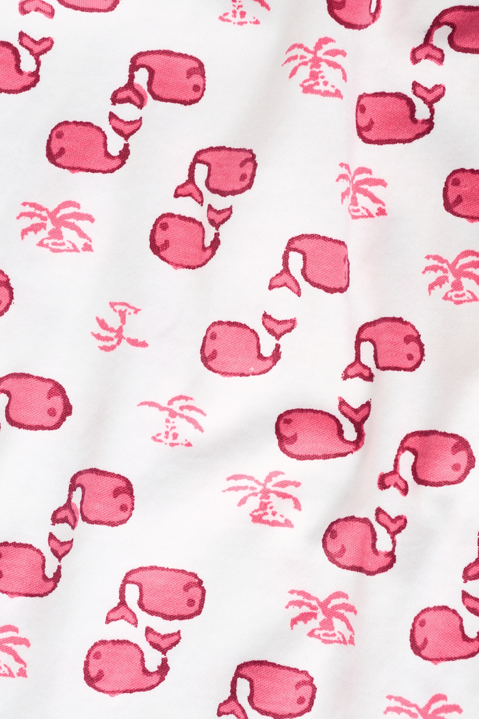 A young child with long brown hair stands barefoot, smiling and wearing the Roller Rabbit Kids Moby Pajamas made from soft Pima cotton, featuring a pink and red mitten pattern, against a plain light background.