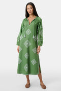 A woman wears the Roller Rabbit Monaco Geo Shiv Caftan in olive green cotton-linen with white embroidery, tassel ties at the neck, and side slits. She stands facing forward with straight dark hair and brown woven flats.