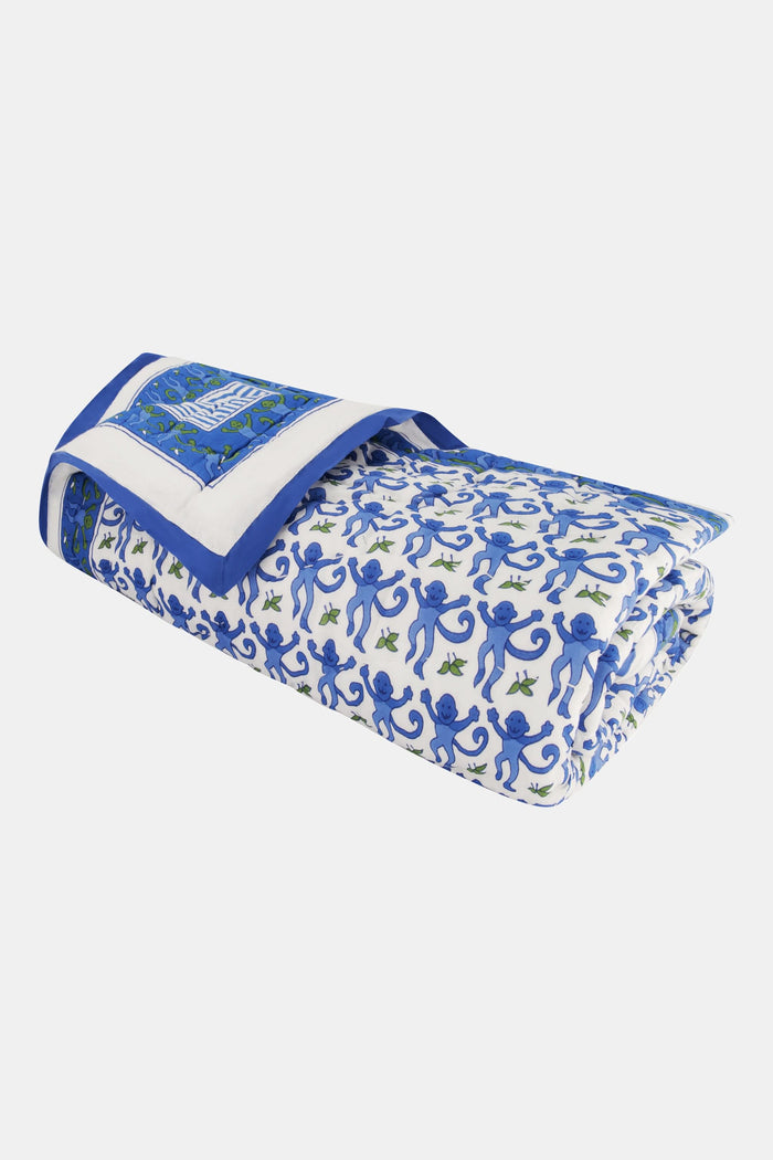 The Roller Rabbit Monkey Baby Quilt is a folded cotton quilt with a white base, blue and green monkey and leaf print, a blue border, and a decorative square featuring an intricate blue and green design.