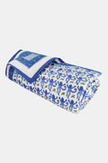 The Roller Rabbit Monkey Baby Quilt is a folded cotton quilt with a white base, blue and green monkey and leaf print, a blue border, and a decorative square featuring an intricate blue and green design.