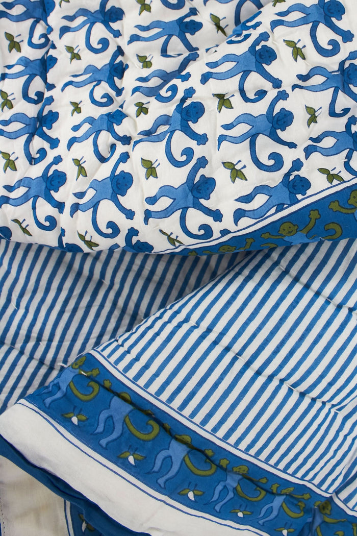 The Roller Rabbit Monkey Baby Quilt is a folded cotton quilt with a white base, blue and green monkey and leaf print, a blue border, and a decorative square featuring an intricate blue and green design.