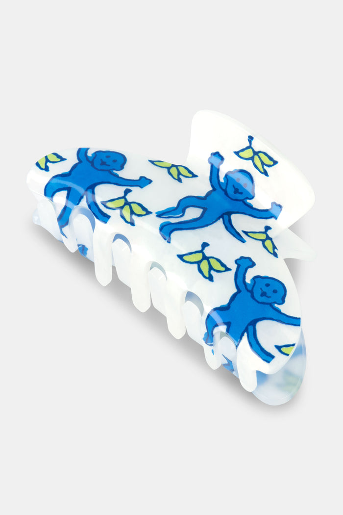 The Roller Rabbit Monkey Claw Clip is a white acrylic hair accessory featuring blue monkeys and small green leaves, displayed on a plain light gray background.