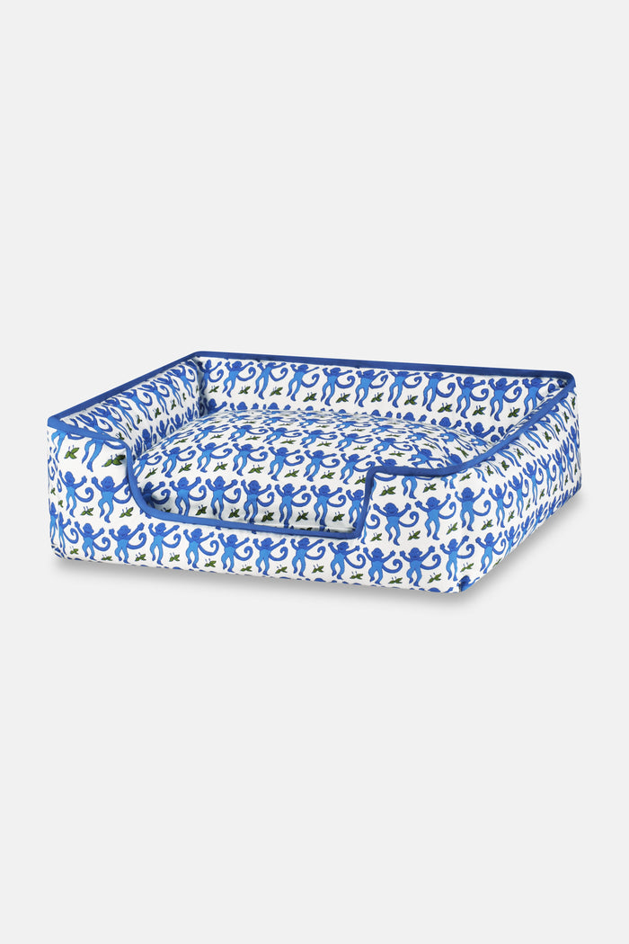 The Roller Rabbit Monkey Dog Bed is a rectangular plush bed with raised sides, a lowered front entrance, and a blue and white abstract pattern. It features machine-washable materials for easy cleaning.