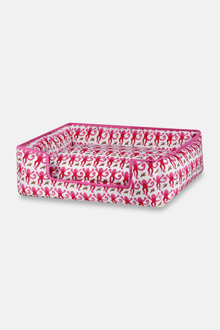 The Roller Rabbit Monkey Dog Bed features a vibrant pink, red, and green monkey print on white, raised sides, a lowered front for easy access, and is machine-washable for your pet's comfort and convenience.