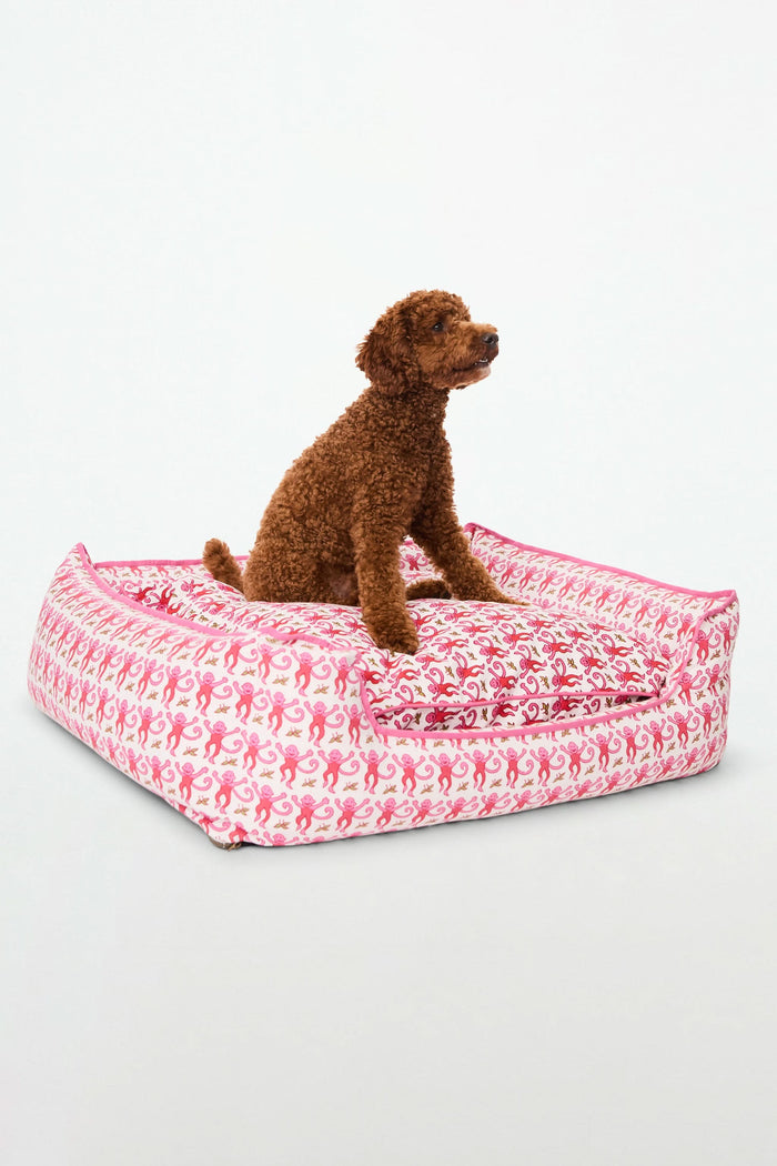 The Roller Rabbit Monkey Dog Bed features a vibrant pink, red, and green monkey print on white, raised sides, a lowered front for easy access, and is machine-washable for your pet's comfort and convenience.