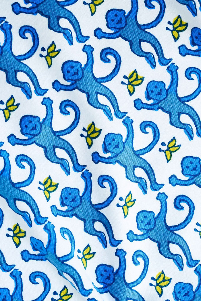 A woman stands barefoot against a plain white background wearing the Roller Rabbit Monkey Fiora Pajamas, a blue-and-white patterned short-sleeve polo pajama set with matching pants.