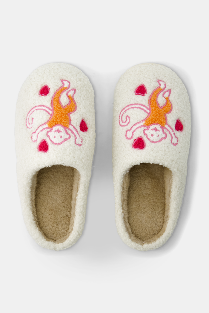 Roller Rabbit’s Monkey Fuzzy Slippers are cream-colored shearling slides with embroidered orange and white cats and red hearts on top, finished with a durable rubber sole.