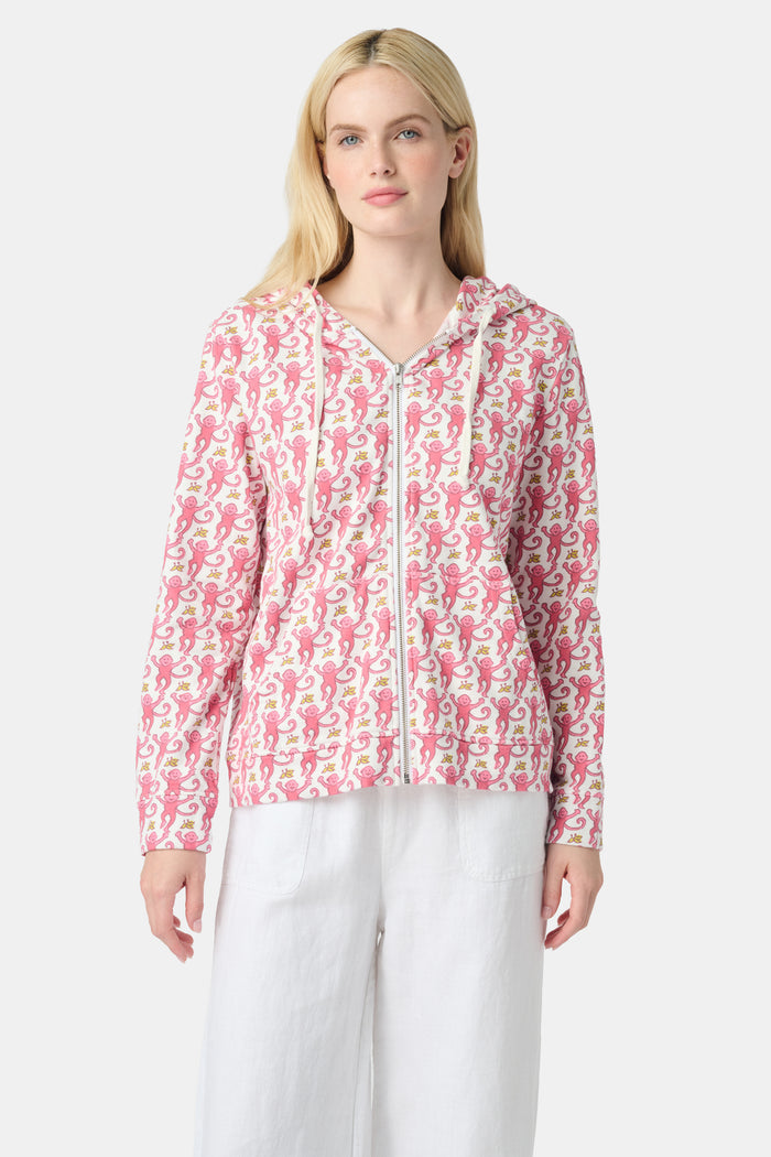 A smiling woman with long blonde hair wears the Roller Rabbit Monkey Harley Hoodie, a white zip-up French terry hoodie with pink seahorse pattern and white drawstrings, paired with white pants against a light background.