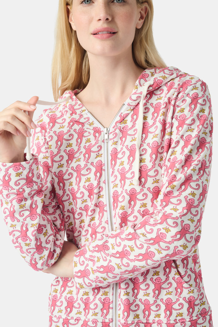 A smiling woman with long blonde hair wears the Roller Rabbit Monkey Harley Hoodie, a white zip-up French terry hoodie with pink seahorse pattern and white drawstrings, paired with white pants against a light background.