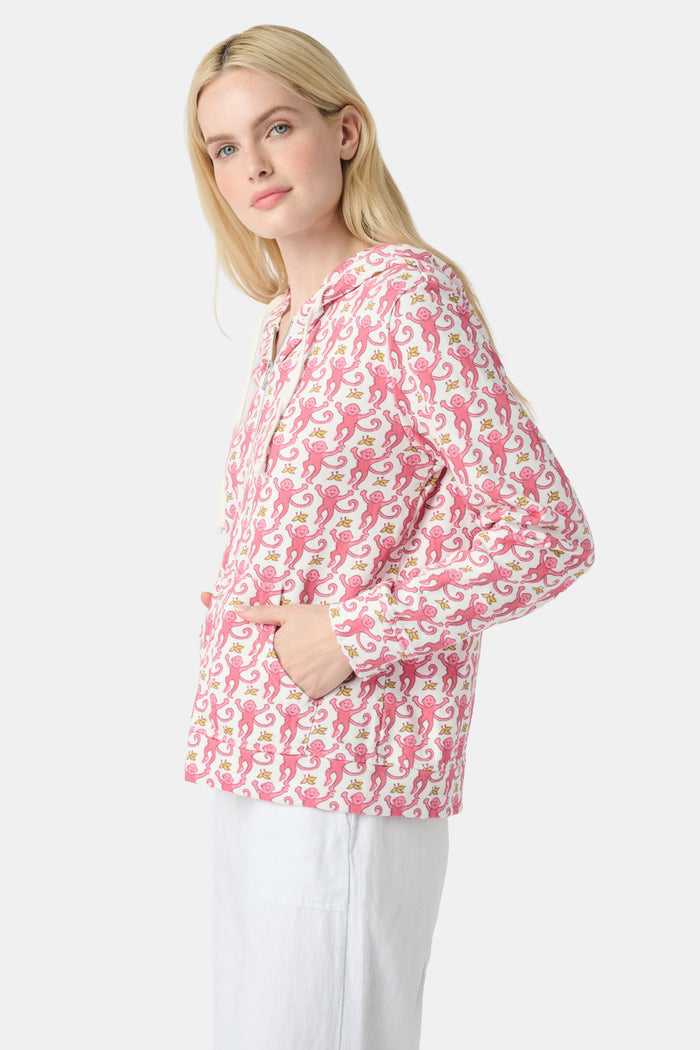 A smiling woman with long blonde hair wears the Roller Rabbit Monkey Harley Hoodie, a white zip-up French terry hoodie with pink seahorse pattern and white drawstrings, paired with white pants against a light background.