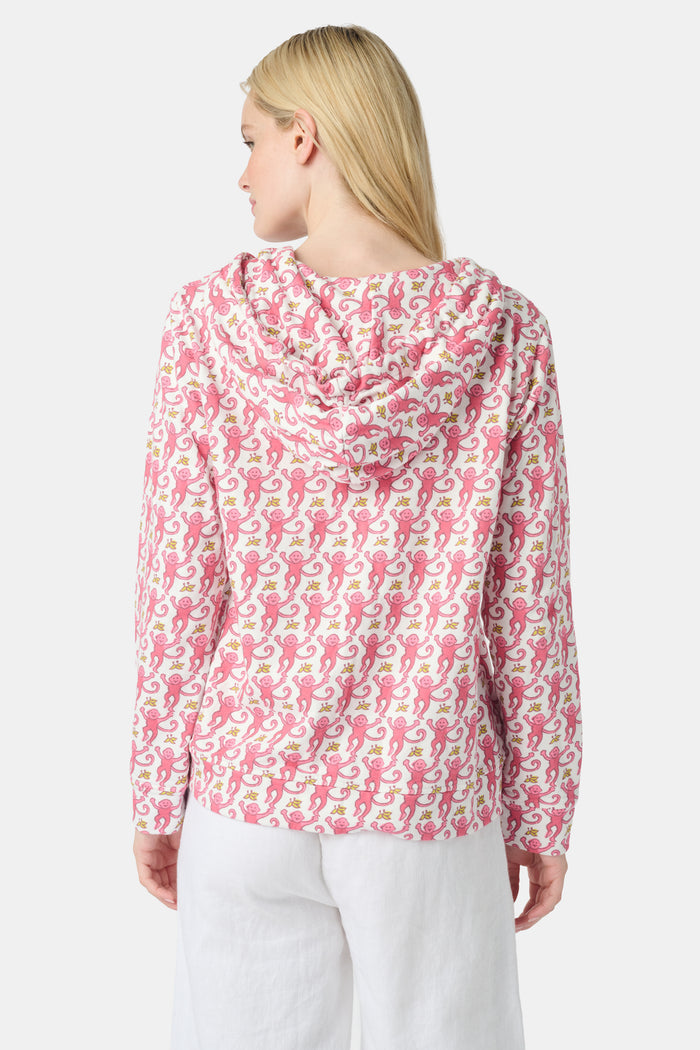 A smiling woman with long blonde hair wears the Roller Rabbit Monkey Harley Hoodie, a white zip-up French terry hoodie with pink seahorse pattern and white drawstrings, paired with white pants against a light background.