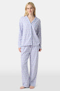 A woman stands barefoot against a plain, light background wearing the Roller Rabbit Monkey Long Sleeve Polo Pajamas, a women's set featuring a button-up top and loose-fitting pants in pima cotton with a light purple and white paisley print.
