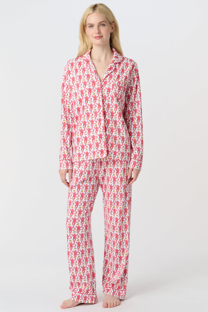 A woman stands barefoot in Roller Rabbit’s Monkey Long Sleeve Polo Pajamas—a matching pink and white Pima cotton set with long sleeves and pants—against a plain white background.
