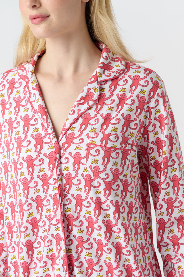 A woman stands barefoot in Roller Rabbit’s Monkey Long Sleeve Polo Pajamas—a matching pink and white Pima cotton set with long sleeves and pants—against a plain white background.